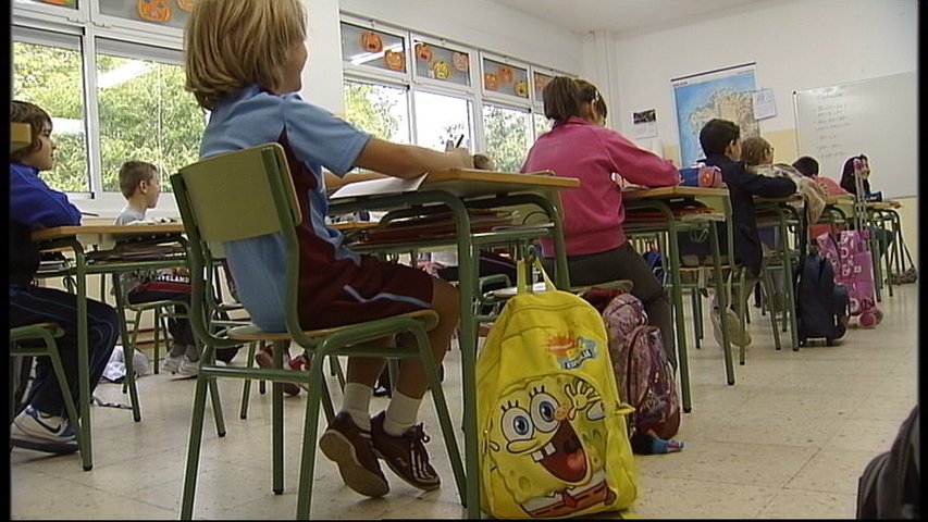 Niños sentados en el colegio con sus mochilas al lado